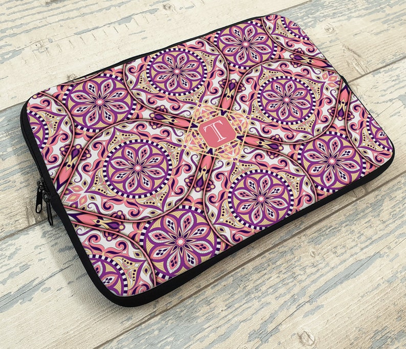 May include: A pink and purple laptop sleeve with a mandala pattern and a gold monogram "T" in the center.