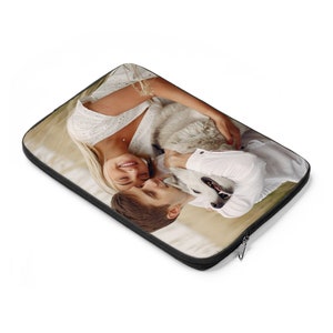 May include: A laptop sleeve with a photo of a couple cuddling a dog. The couple is wearing white shirts and the dog is white with black markings.