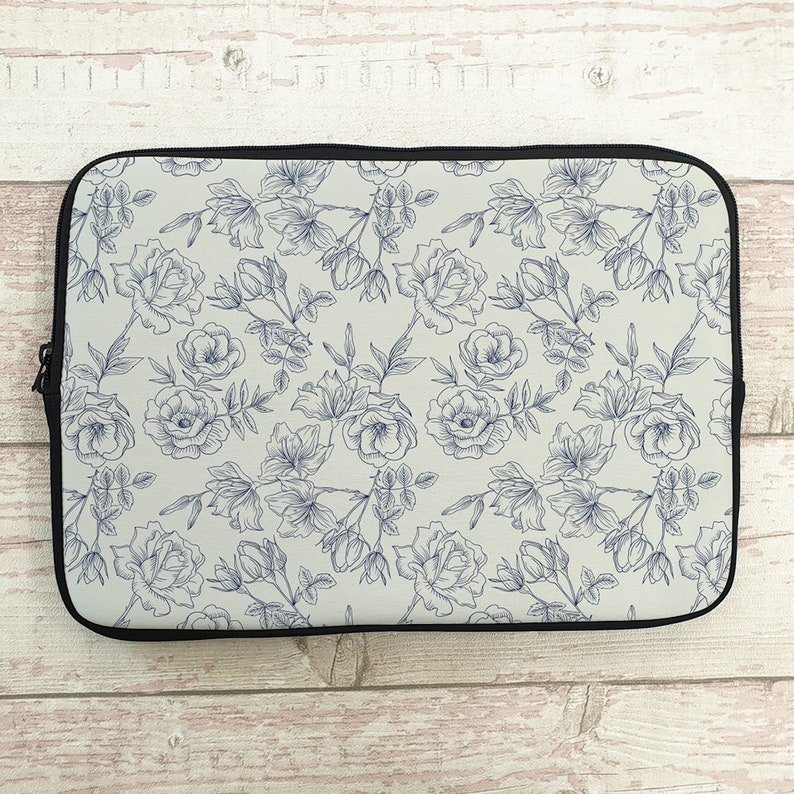 May include: A white laptop sleeve with a blue floral pattern. The pattern features delicate line drawings of roses and leaves.