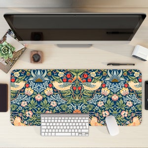 Può includere: Un tappetino da scrivania blu e verde con un design floreale e di uccelli. Il tappetino è su una scrivania di legno con una tastiera, un mouse e altri articoli da ufficio.