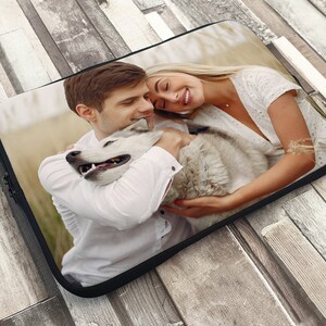 May include: A couple and their dog are hugging in a field. The man is wearing a white shirt and the woman is wearing a white dress. The dog is a white husky.