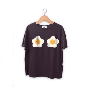 May include: A black t-shirt with a graphic of two smiling fried eggs. The eggs are white with yellow yolks and are positioned side-by-side on the shirt.