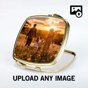 May include: A gold compact mirror with a photo of a family of four walking in a field at sunset. The mirror is open and the reflection is visible.