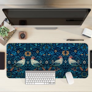 May include: A blue and green patterned desk mat with a white keyboard and a white mouse. The pattern features stylised birds and flowers.