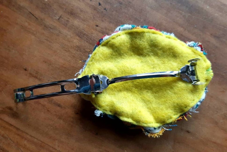 May include: A yellow felt hair clip with a colorful fabric trim and a silver metal clip.