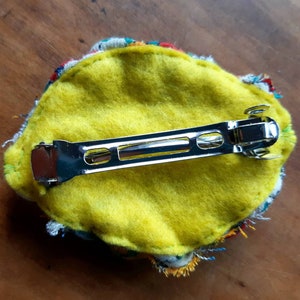 May include: A yellow felt hair clip with a colorful fabric trim and a silver metal bar clip.