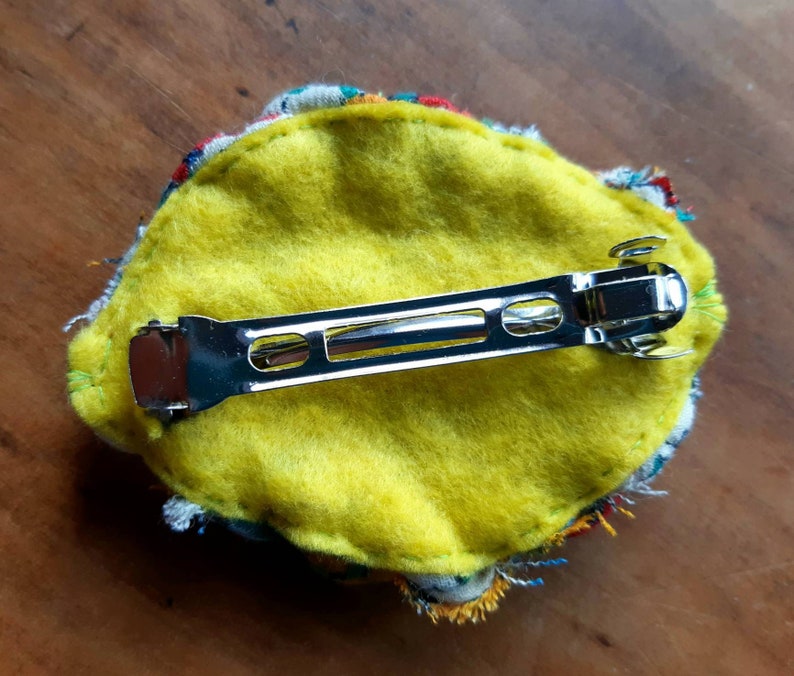 May include: A yellow felt hair clip with a colorful fabric trim and a silver metal bar clip.