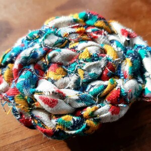 May include: A colorful fabric ball made from scraps of fabric in shades of red, blue, yellow, and white. The fabric is woven together to create a unique and textured ball.
