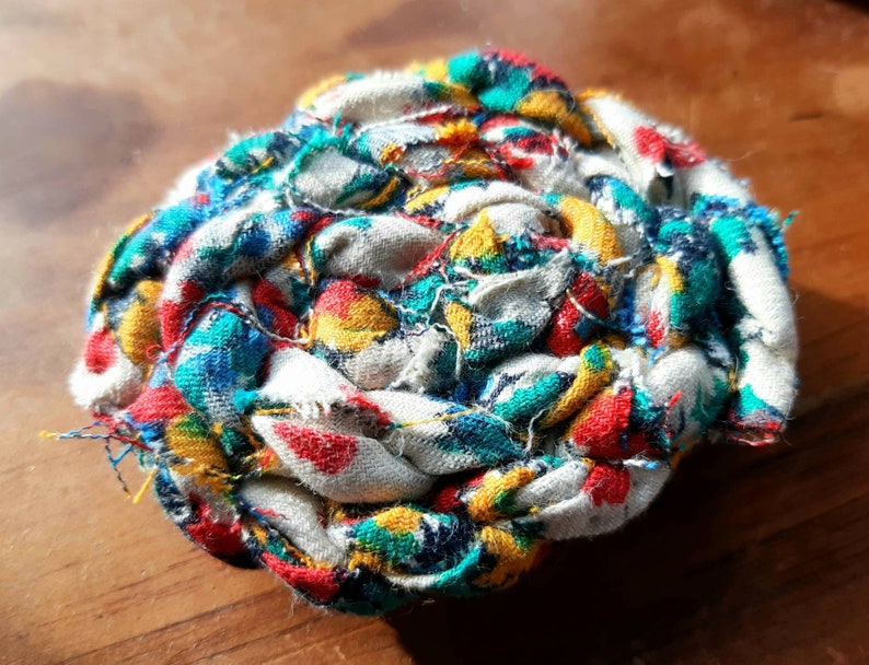 May include: A colorful fabric ball made from scraps of fabric in shades of red, blue, yellow, and white. The fabric is woven together to create a unique and textured ball.