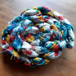 May include: A colorful fabric ball made from scraps of fabric in shades of blue, red, yellow, and white. The fabric is woven together to create a ball shape.