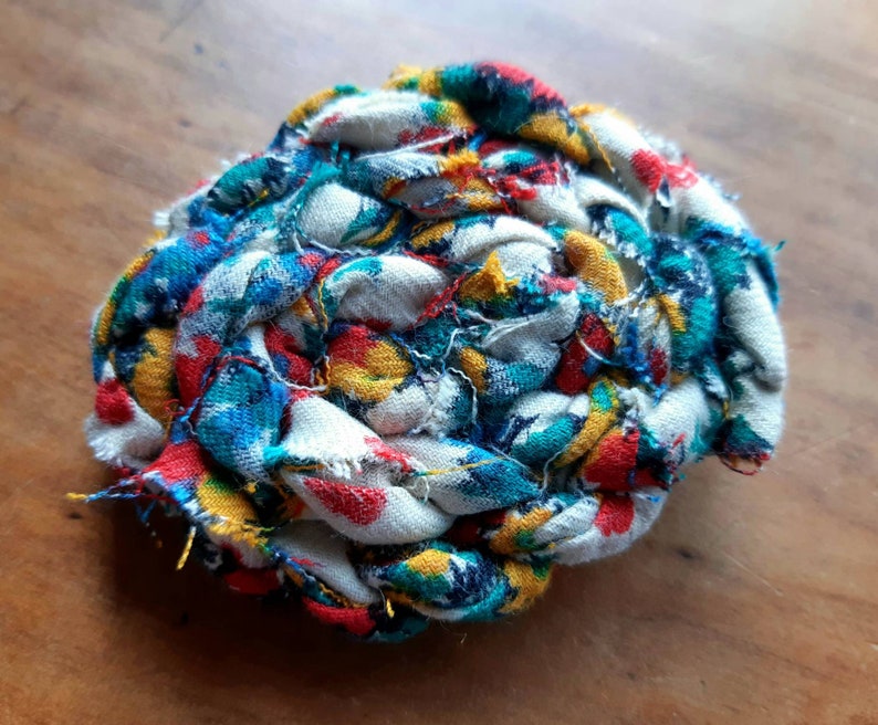 May include: A colorful fabric ball made from scraps of fabric in shades of blue, red, yellow, and white. The fabric is woven together to create a ball shape.