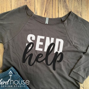 May include: A charcoal gray long-sleeve shirt with the text "SEND help" printed in white and black. The text is in a bold, stylized font.