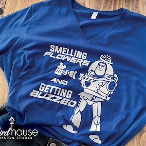 May include: A blue t-shirt with a white graphic of Buzz Lightyear from Toy Story. The graphic says "Smelling Flowers and Getting Buzzed".
