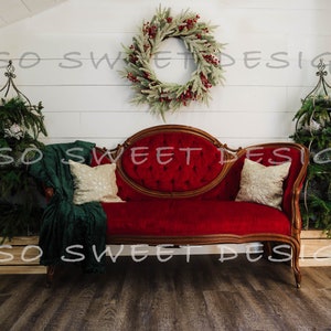 Puede incluir: Un sofá de terciopelo rojo con botones, cojines dorados y una manta verde se encuentra frente a una pared de madera blanca con una corona de Navidad encima. Dos árboles de Navidad están en las esquinas de la habitación.