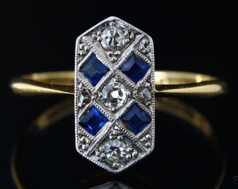 May include: A gold ring with a rectangular center stone set with blue sapphires and diamonds in a geometric pattern.