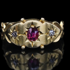 May include: A gold ring with a red ruby and two smaller diamonds set in a starburst design.