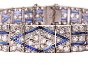 Könnte beinhalten: Nahaufnahme eines Art-Deco-Armbands mit geometrischem Design. Das silberfarbene Armband hat klare, rund geschliffene Steine und leuchtend blaue rechteckige und rautenförmige Akzente. Der Verschluss ist oben sichtbar.