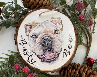 May include: A round wooden bauble featuring a painted portrait of a bulldog. The bauble is decorated with the dog's name, "Busty Boo", written in cursive.