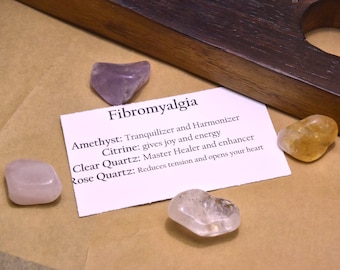 May include: A white card with the text "Fibromyalgia" and descriptions of the healing properties of amethyst, citrine, clear quartz, and rose quartz crystals. The card is surrounded by four crystals: amethyst, citrine, clear quartz, and rose quartz.