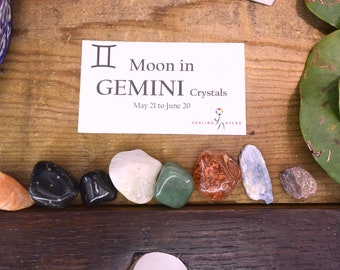 May include: A set of crystals for the Gemini zodiac sign, May 21 to June 20. The crystals are arranged in a row on a wooden surface. The crystals are various colors, including orange, black, white, green, red, blue, and gray.