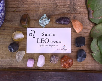May include: A set of crystals for Leo zodiac sign, July 23 to August 22. The crystals are arranged on a wooden surface with a card that reads "Sun in LEO Crystals" and "July 23 to August 22".