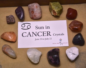 May include: A collection of crystals for the zodiac sign Cancer, with the text "Sun in CANCER Crystals June 21 to July 22 Healing Atlas". The crystals are arranged in a circle around the text, and include a variety of colors and shapes.