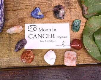 May include: A set of crystals for the zodiac sign Cancer, with the text "Moon in Cancer Crystals June 21 to July 22" on a white card. The crystals are a variety of colors and shapes, including pink, green, red, orange, white, and blue.