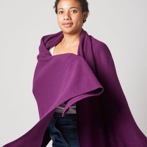 May include: A purple knitted scarf draped around a person's shoulders. The scarf is soft and flowing, and the color is rich and vibrant.