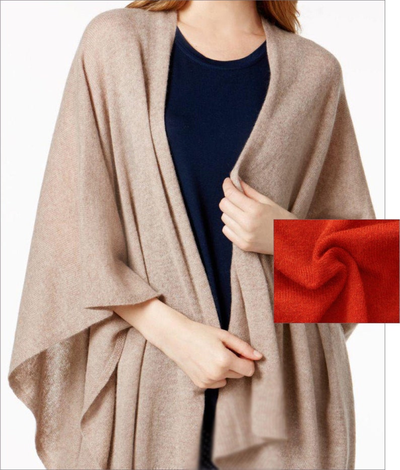 May include: A beige knitted shawl with a draped design. The shawl is made of a soft, lightweight fabric and has a relaxed fit.