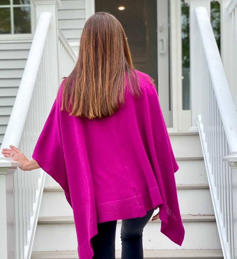 May include: A woman wearing a magenta knitted poncho with a long, straight hairstyle. The poncho has a loose fit and a slightly asymmetrical hemline.