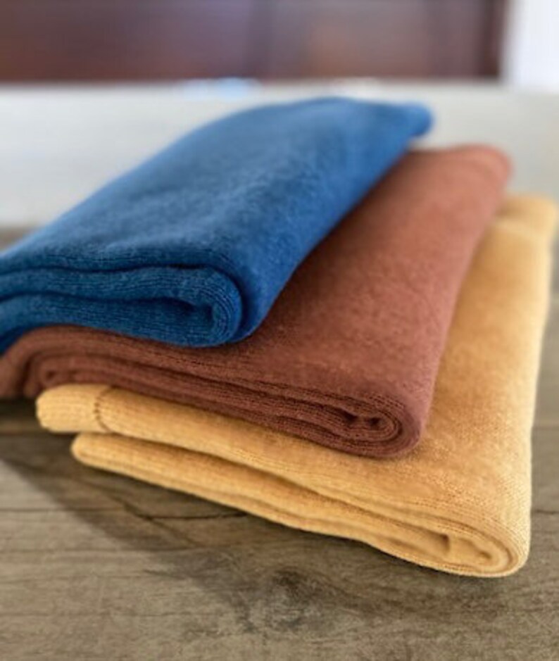 May include: Three folded fabric blankets in different colors: a dark blue, a rust brown, and a light yellow.