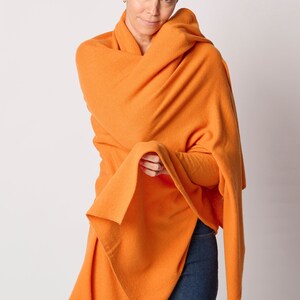 May include: A bright orange knitted wrap or shawl is draped around a person's shoulders. The wrap is folded over itself and the ends are hanging down.