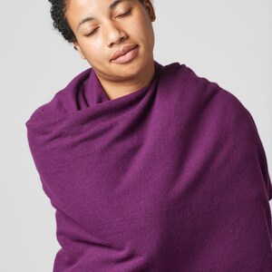 May include: A person with short curly hair is wrapped in a deep purple shawl. The person has their eyes closed and is looking down.