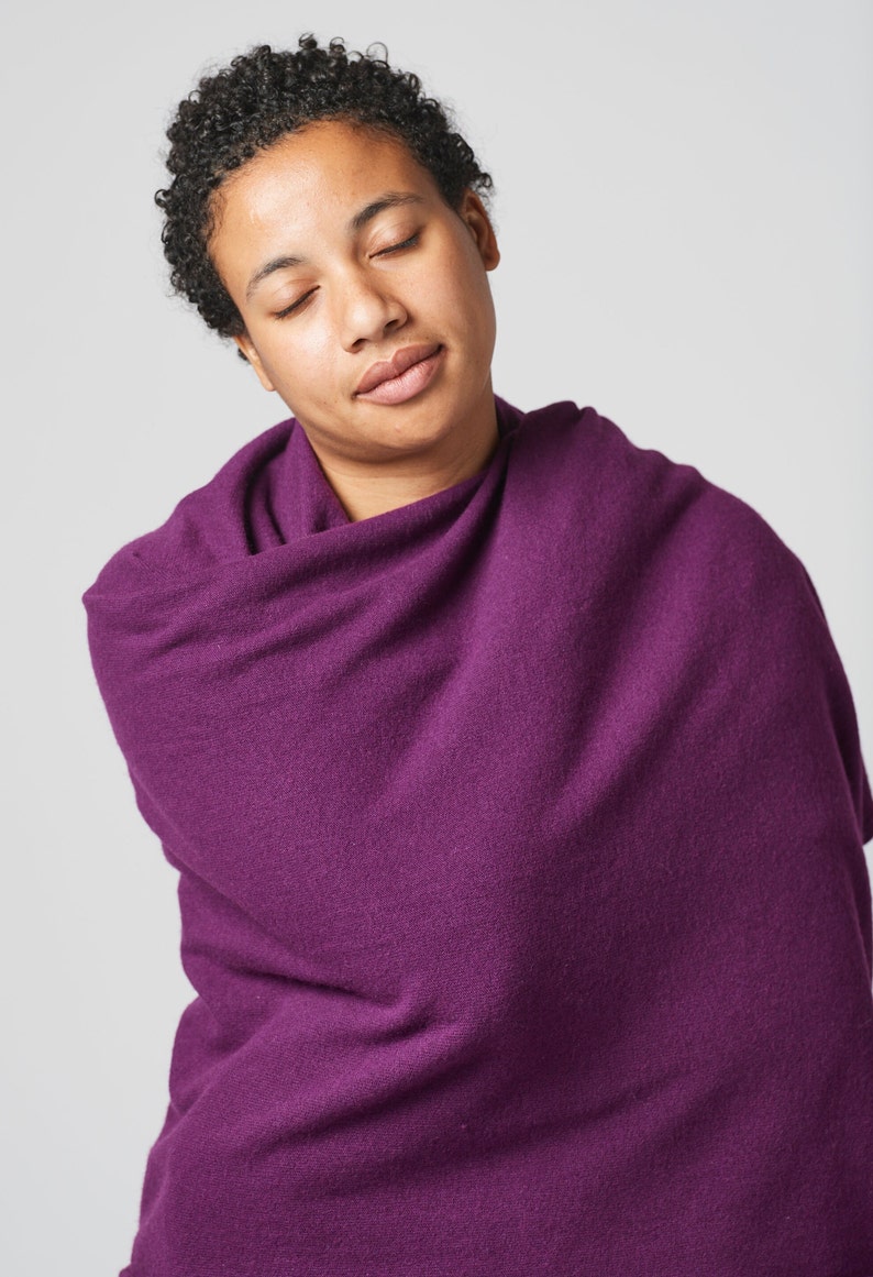 May include: A person with short curly hair is wrapped in a deep purple shawl. The person has their eyes closed and is looking down.