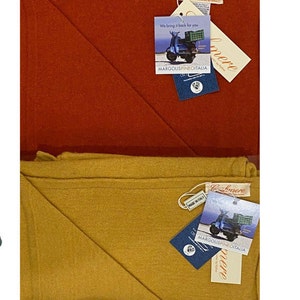 May include: Four folded cashmere scarves in teal, red, mustard yellow, and purple. Each scarf has a tag with a scooter and the text "We bring it back for you" and "MARGOLISPINEOITALIA".