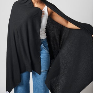 May include: A black knitted scarf draped over a person's shoulders. The scarf is made of a soft, lightweight fabric and has a simple, elegant design.