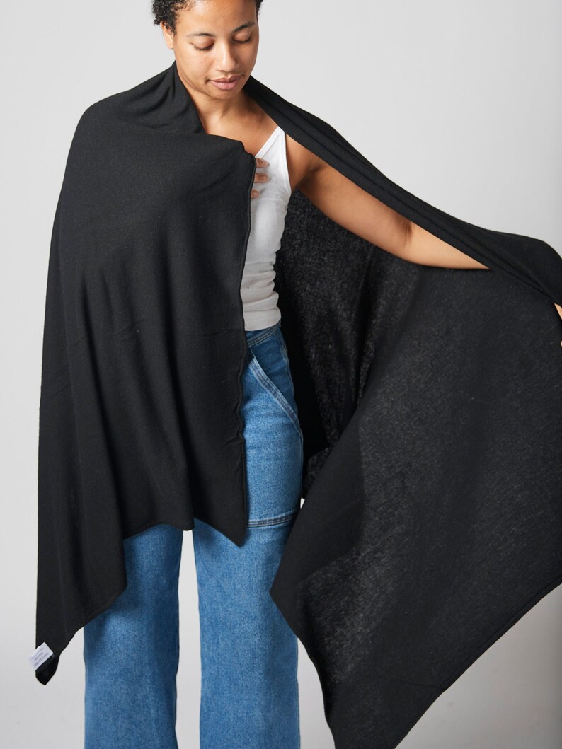 May include: A black knitted scarf draped over a person's shoulders. The scarf is made of a soft, lightweight fabric and has a simple, elegant design.