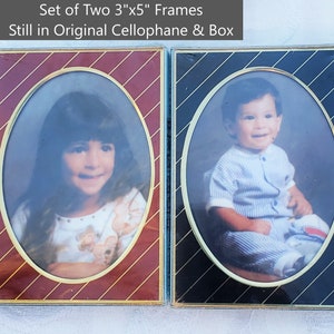 May include: Set of two 3"x5" picture frames, still in original cellophane and box. One frame has a burgundy background with gold diagonal stripes, the other has a black background with gold diagonal stripes. Each frame has an oval photo.