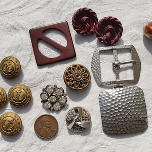 May include: A white ceramic mug with a black handle and the text "But First, Coffee" in a black, bold font. The mug is on a white surface. The mug is approximately 10 cm tall.