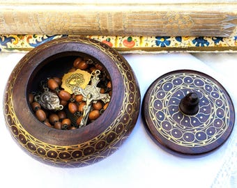 Op de afbeelding: Een houten doos met een deksel, ingewikkeld gesneden met gouden accenten. De doos is open en onthult een rozenkrans met bruine kralen en een zilveren kruisbeeld.