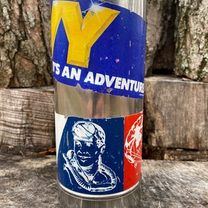 May include: A stainless steel water bottle with two stickers. The top sticker has a yellow "Y" on a blue background with the text "IT'S AN ADVENTURE". The bottom sticker features a diver illustration and a red and white design.