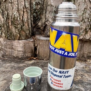 May include: A stainless steel thermos with a blue and yellow sticker that reads "NAVY, NOT JUST A JOB, IT'S..." and "Join Our NAVY Bomb Disposal Team... Explosive Ordnance Disposal". Includes a cup and lid.