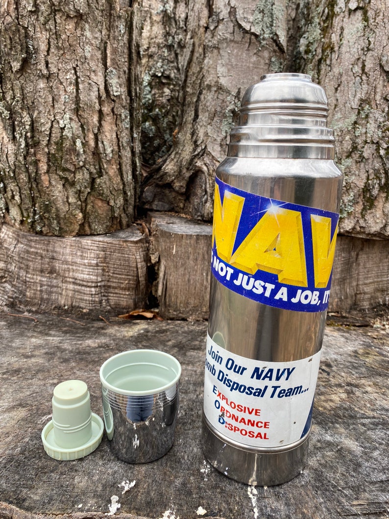 May include: A stainless steel thermos with a blue and yellow sticker that reads "NAVY, NOT JUST A JOB, IT'S..." and "Join Our NAVY Bomb Disposal Team... Explosive Ordnance Disposal". Includes a cup and lid.