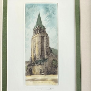 May include: A framed print of a church in Paris, France. The artwork features a tall stone building with a green-roofed spire, set against a light blue sky. The print is in a white mat with a green frame.
