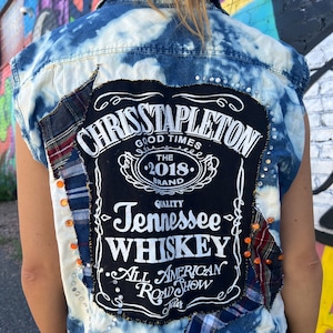 May include: A blue denim vest with patches, rhinestones, and a black patch with the text "Chris Stapleton Good Times The 2018 Brand Quality Tennessee Whiskey All American Road Show Tour".