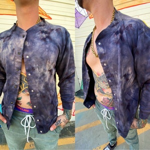 May include: A dark blue tie-dye bomber jacket with a snap button closure. The jacket has a relaxed fit and a slightly oversized look.