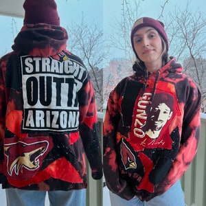 May include: Two red and black hooded sweatshirts with patchwork designs. One sweatshirt has the text "Straight Outta Arizona" and the other has the text "Gunzo" and a cartoon face.
