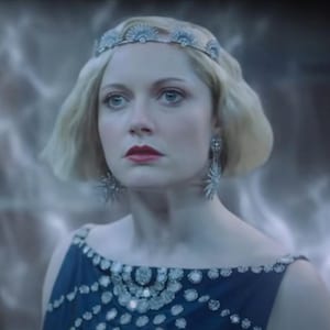 Puede incluir: Una mujer con cabello rubio lleva una tiara plateada y pendientes en forma de estrella. Lleva un vestido azul oscuro con adornos plateados alrededor del escote. La imagen tiene una cualidad suave y et&eacute;rea.
