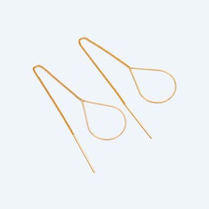 Può includere: Un paio di orecchini a filo color oro. Ogni orecchino presenta una cornice a forma di goccia sospesa da una delicata catena. Un perno dritto e sottile si estende dalla parte inferiore della goccia, progettato per essere inserito nell'orecchio.