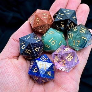 May include: A set of seven gemstone dice, each with a different color and mineral. The dice are in the shape of a d20, with numbers 1-20 printed on each face. The colors of the dice are: red, black, green, blue, purple, and brown.